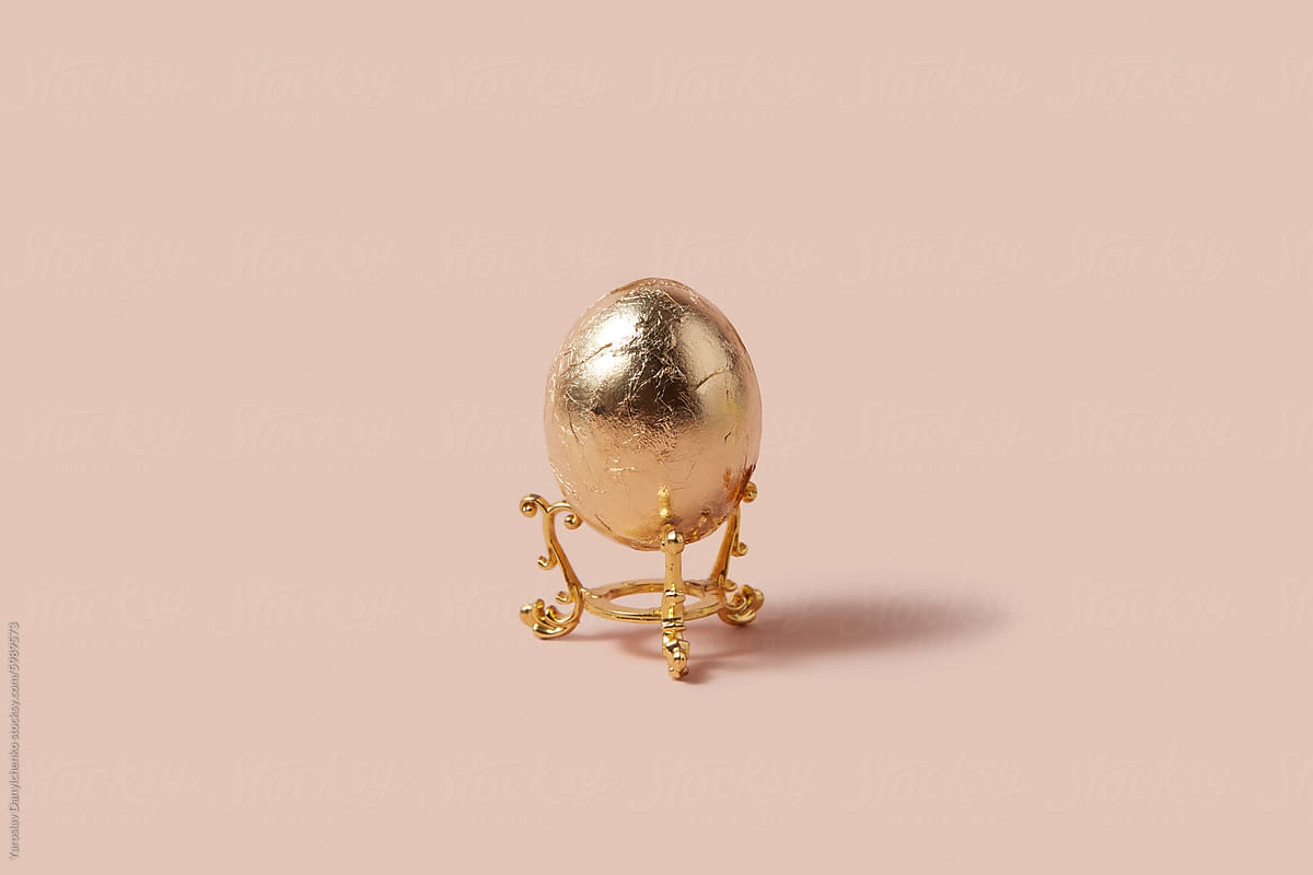 Painted egg placed on golden elegant stand over pink background