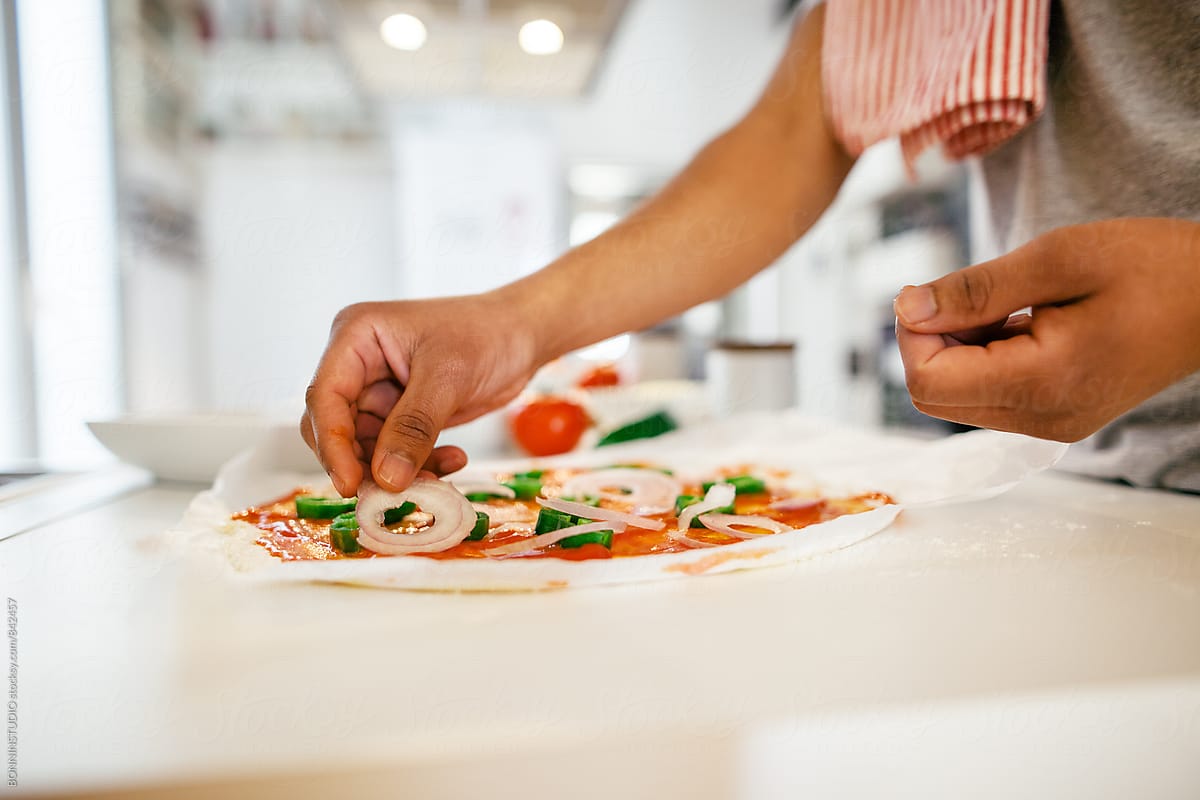 Side view of a man preparing a handmade Italian pizza in the kitchen.