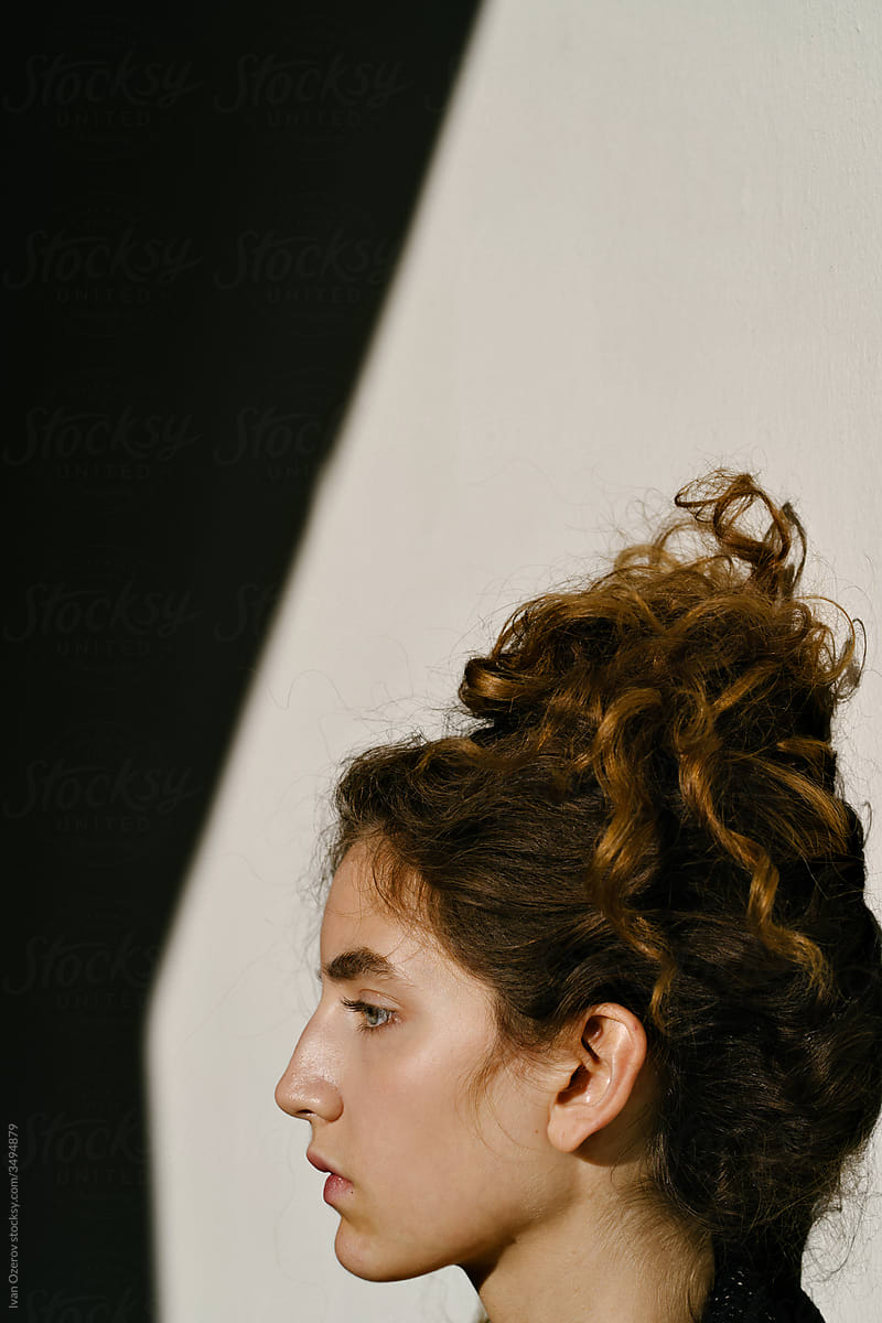 curly-haired woman stands with her back against the wall