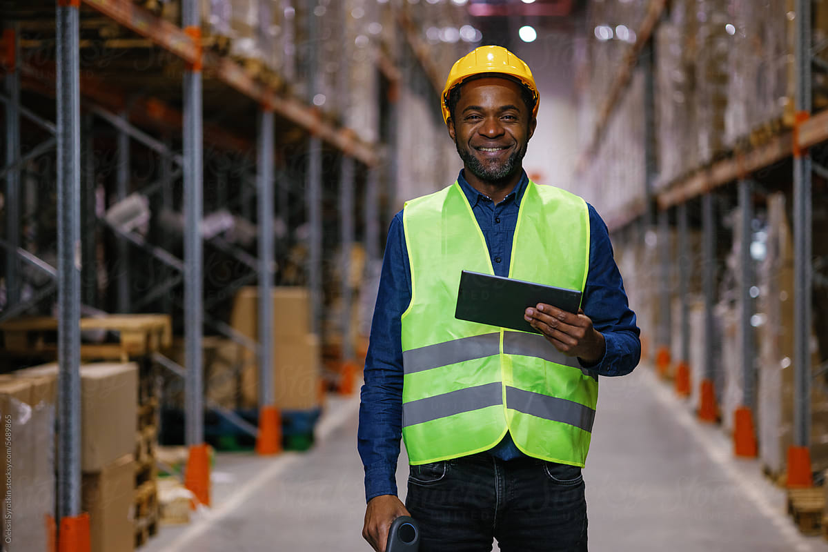 Black warehouse worker tablet storage aisle wearing uniform