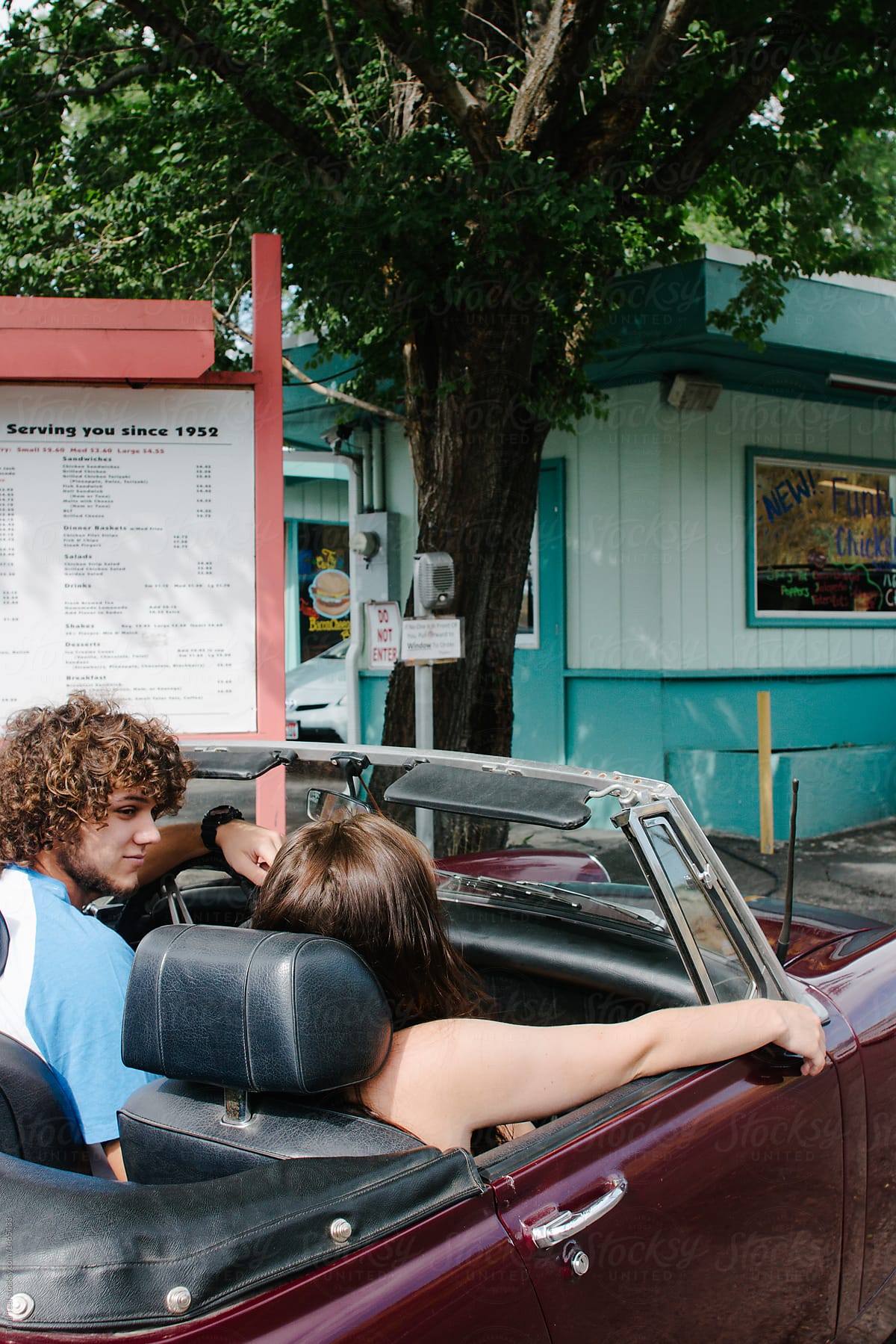 couple sit in convertible in line at fast foot drive thru restaurant