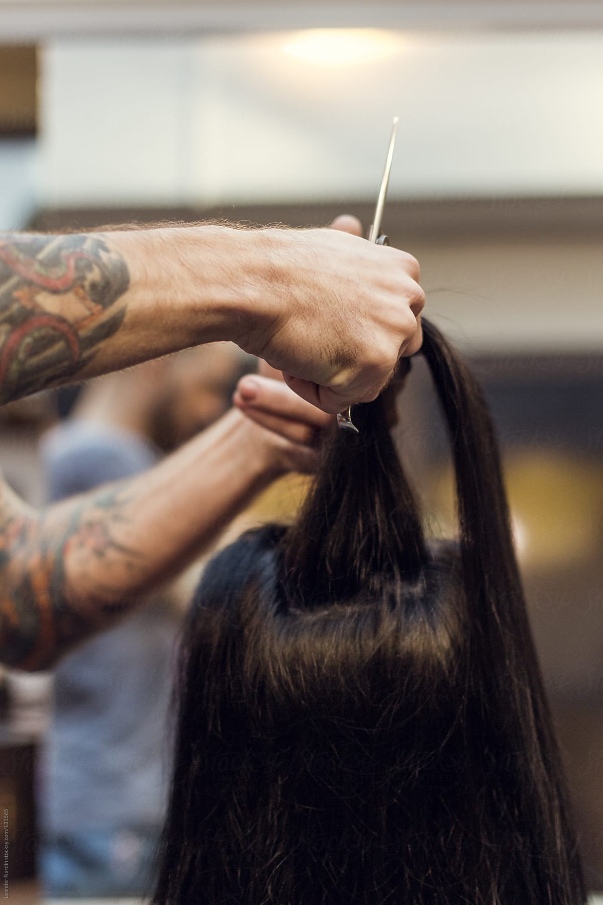 woman is getting her long hair cut by a tattoed hairdresser