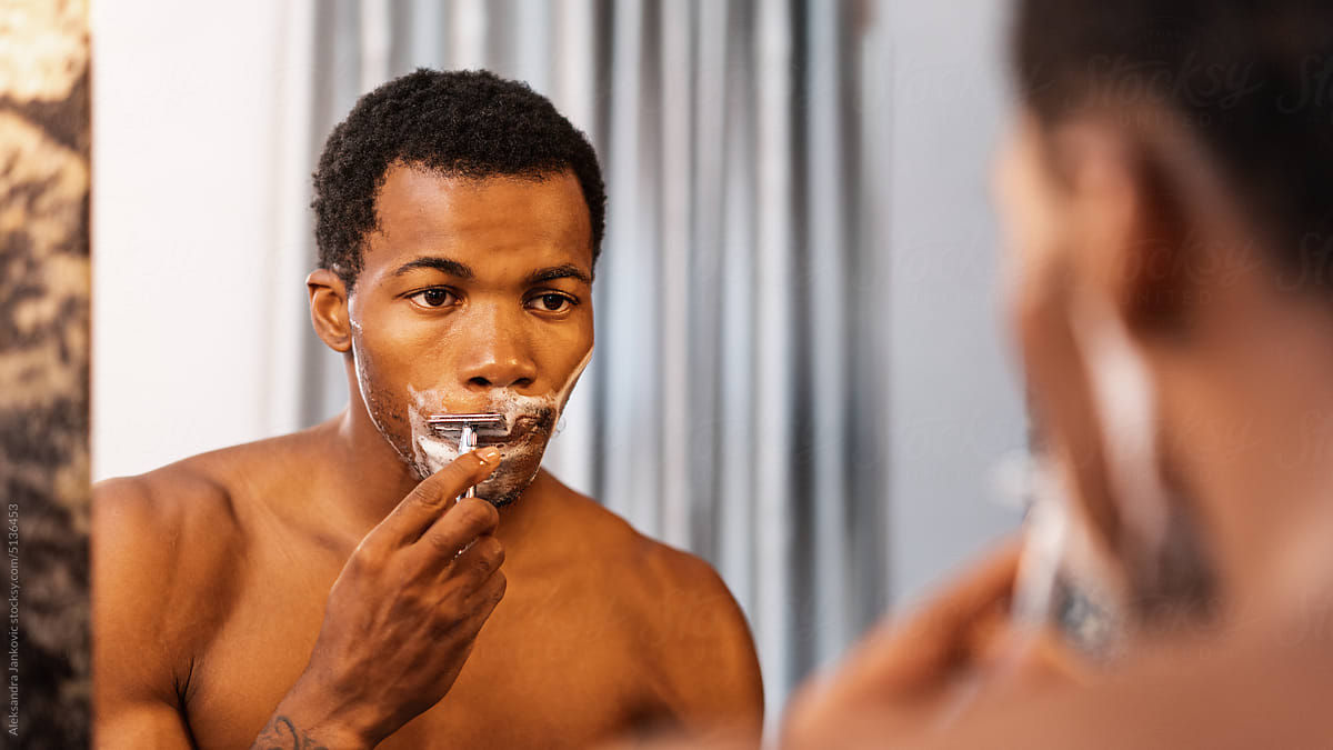 Shirtless Man Shaving And Looking Himself In The Mirror
