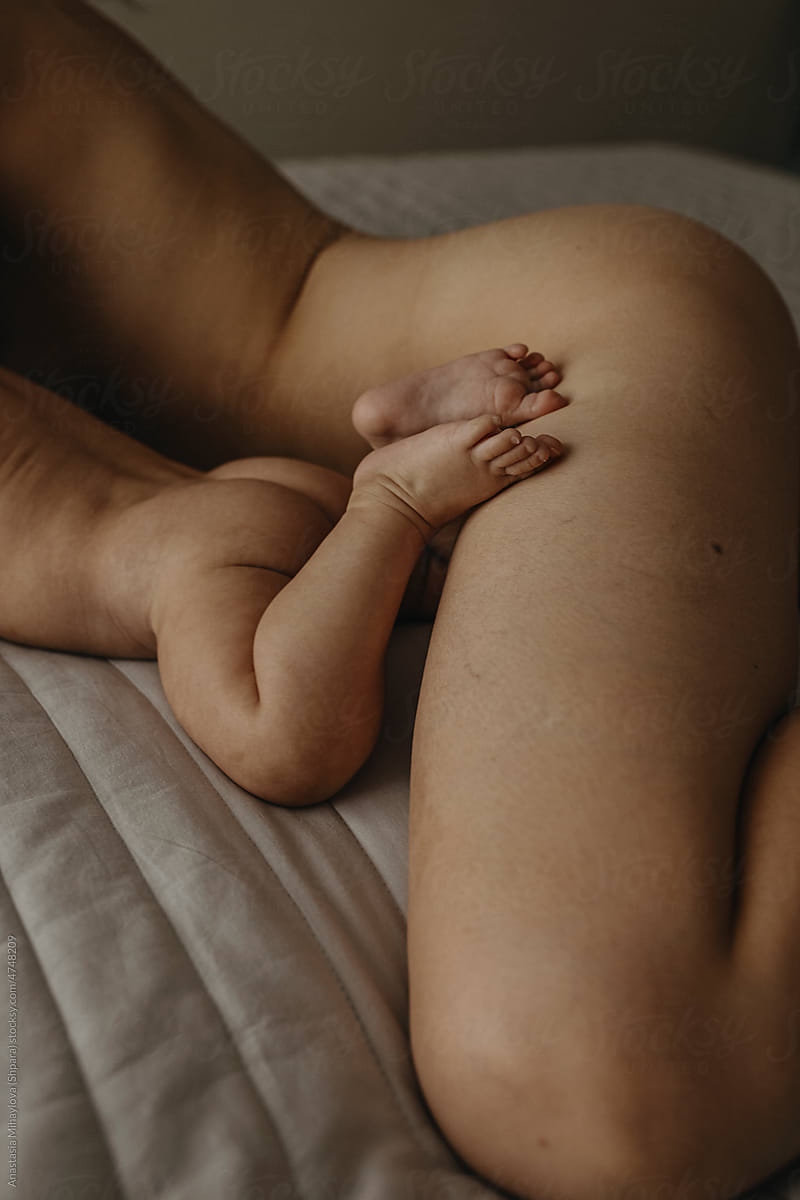 The naked infant is lying on the bed near it\'s naked mother
