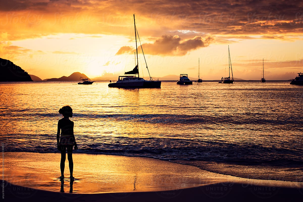 A child watching sailboats on the sea at sunset