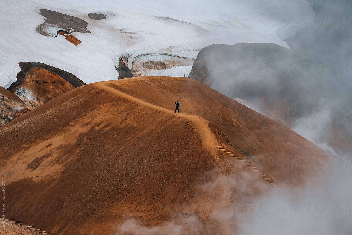 Hiker exploring golden brown landscape of Iceland's geothermal area.