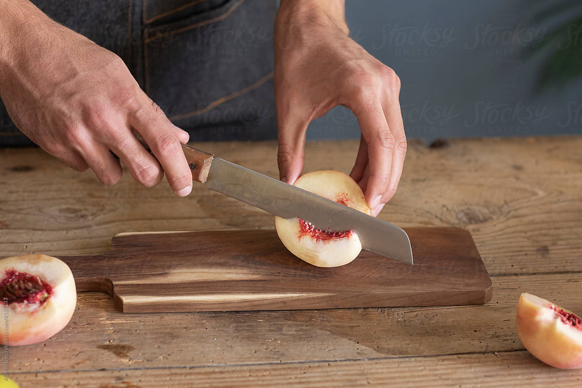 Man\'s Hands Cutting Fresh Peach On Wooden Board