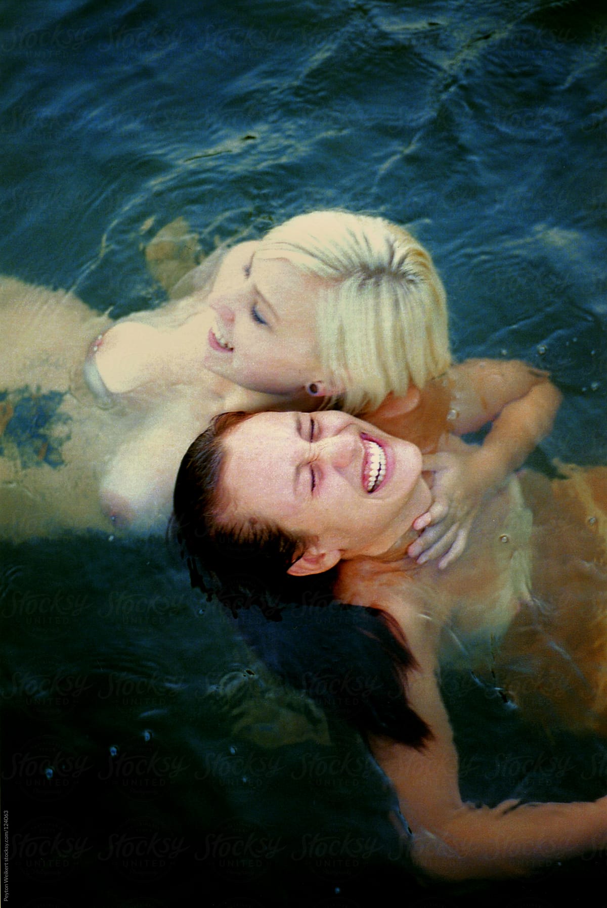 two nude young woman laugh in the water