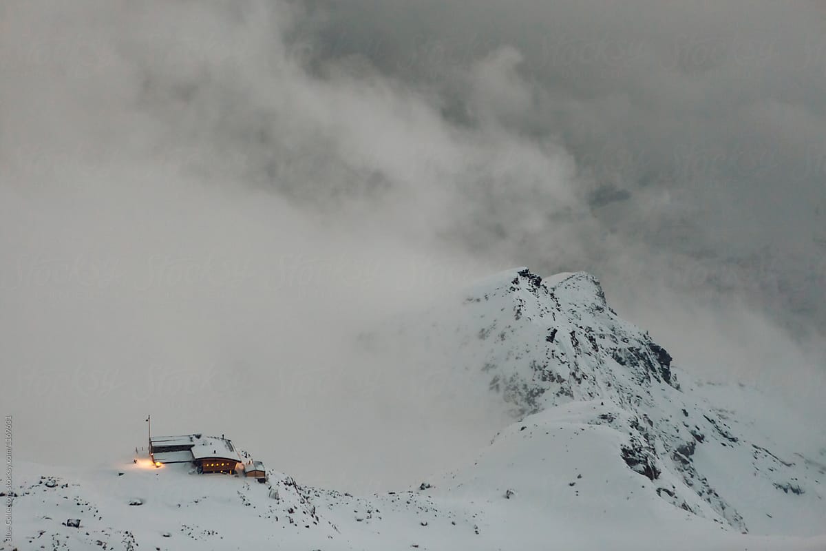 Winter mountain cabin covered in snow in the top of the Alpine mountains, at stormy night