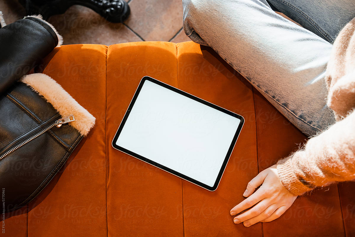 A tablet with a white screen on the sofa next to a woman
