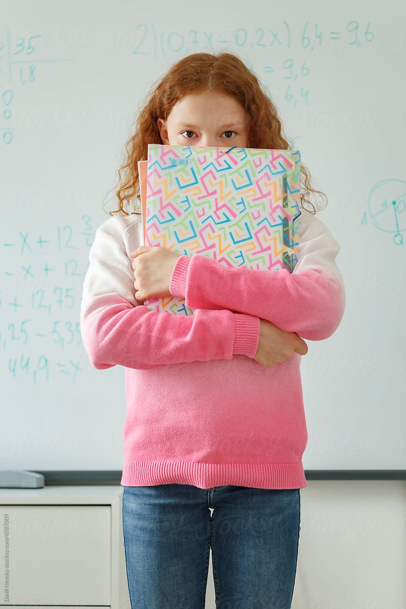 Shy schoolgirl with notepads near whiteboard