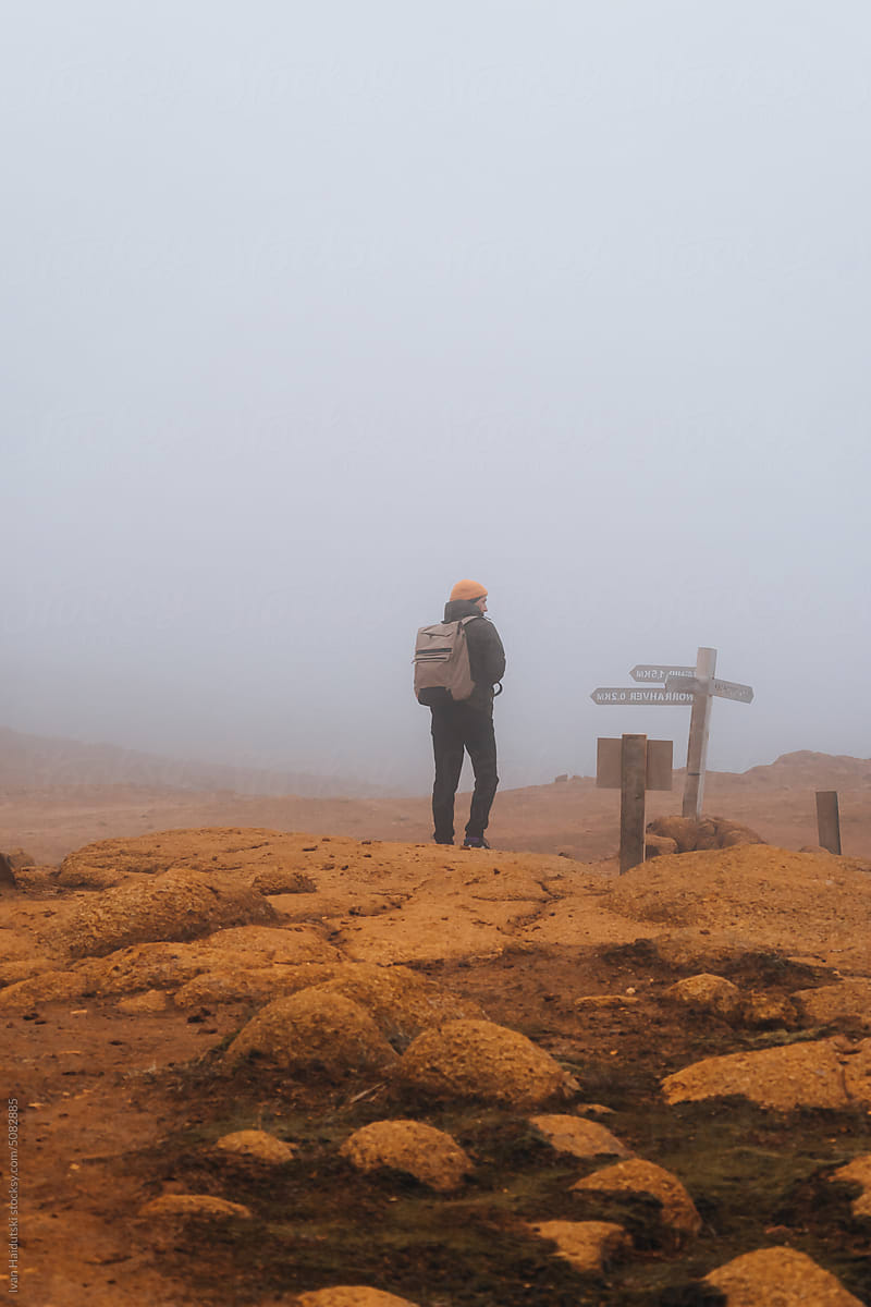 Man From Behind With Orange Cap Hiking In Foggy Rugged Mountains