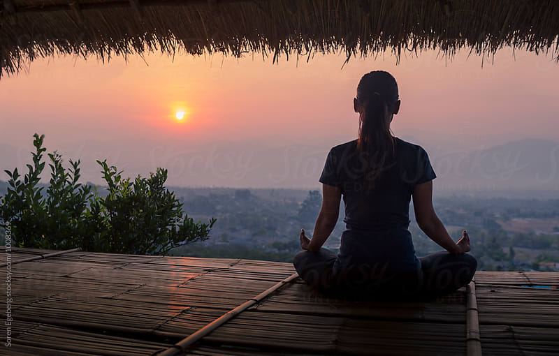 Woman meditating with view of rising sun over the mountains