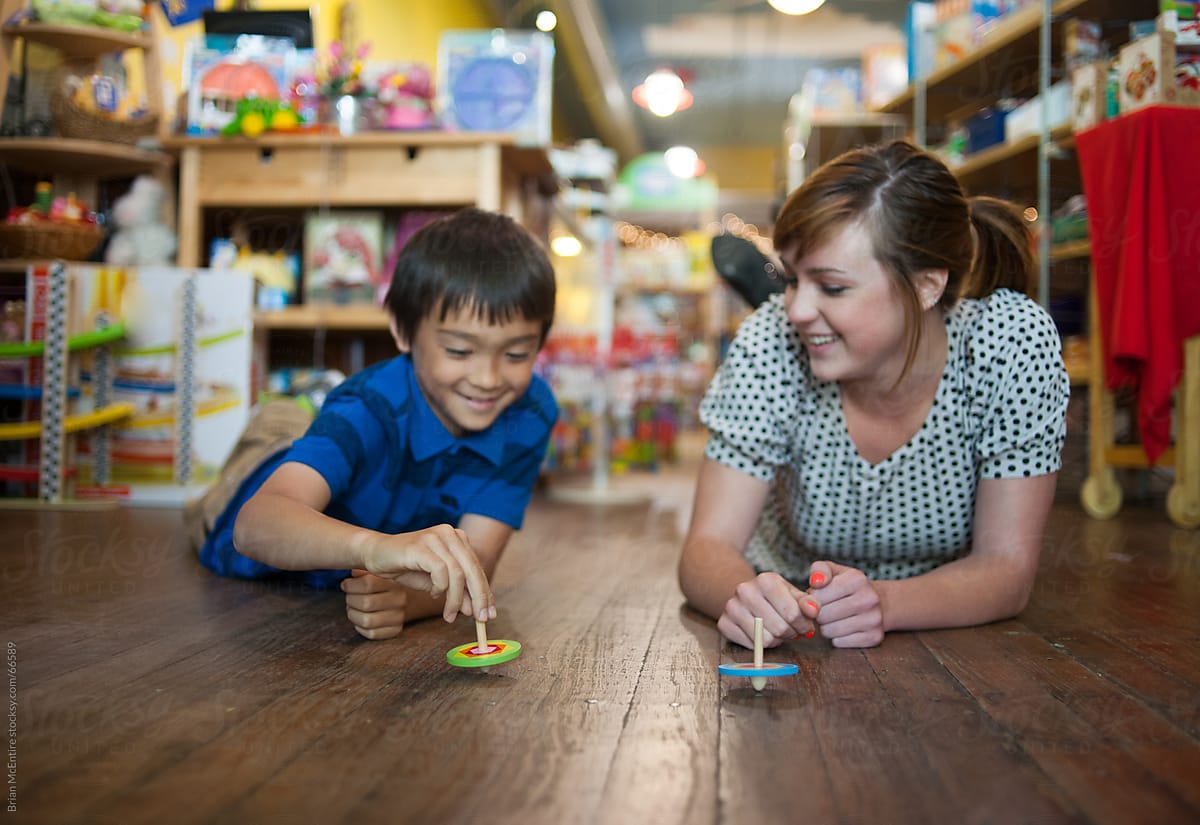 Little Asian boy and store clerk play with toys on the shop floo
