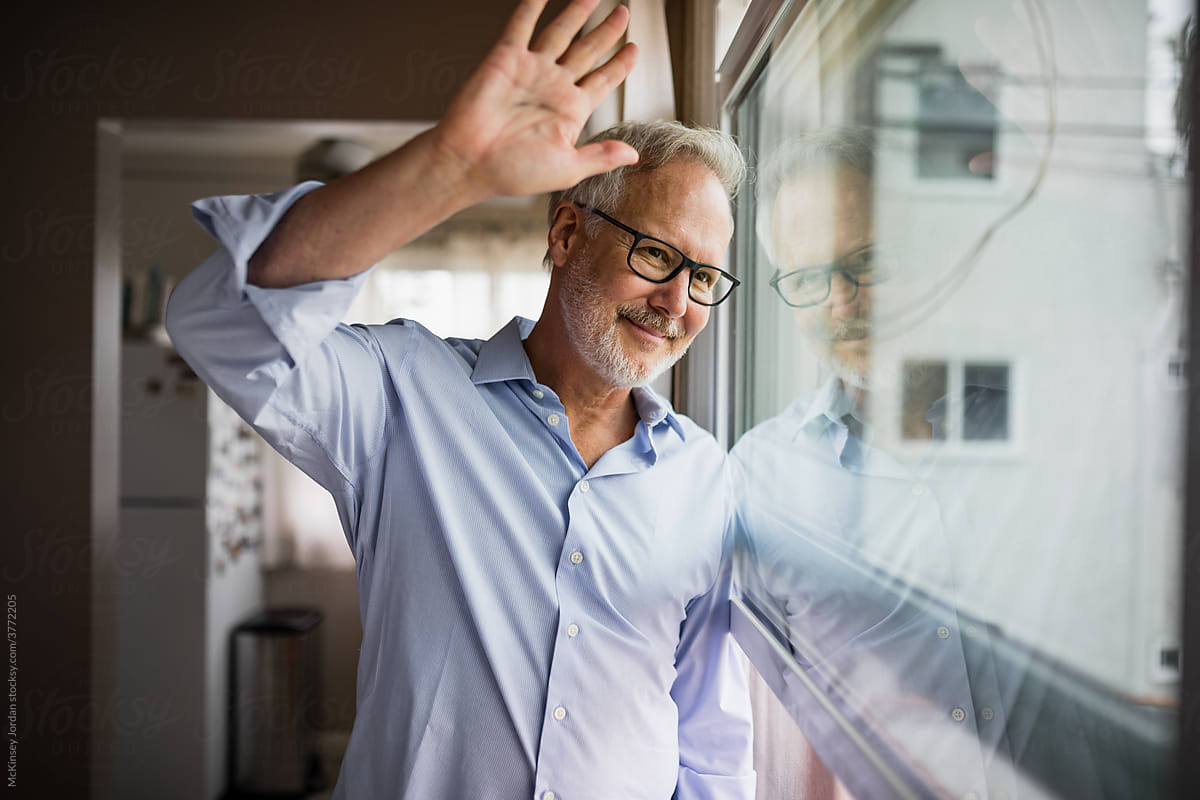Older Gentleman Waves While Looking Out His Apartment Window