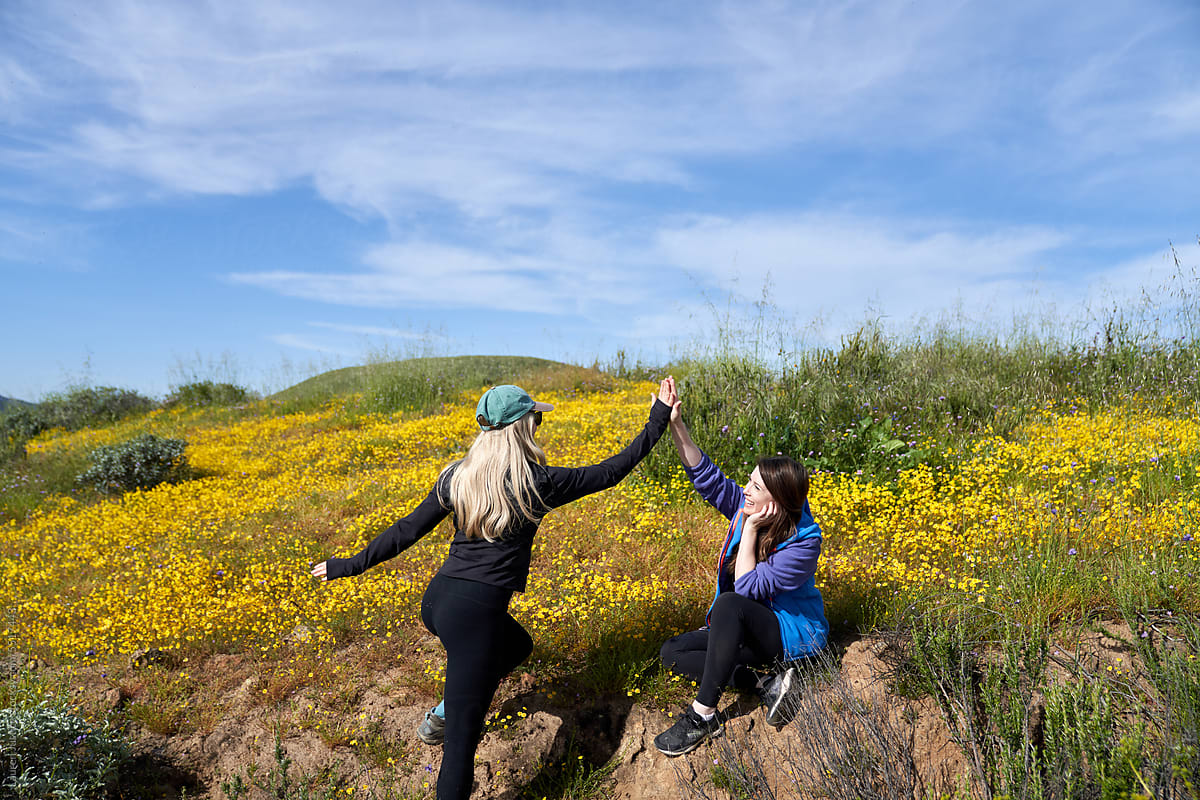 Two girls greet each other with a high five in a field of flowers