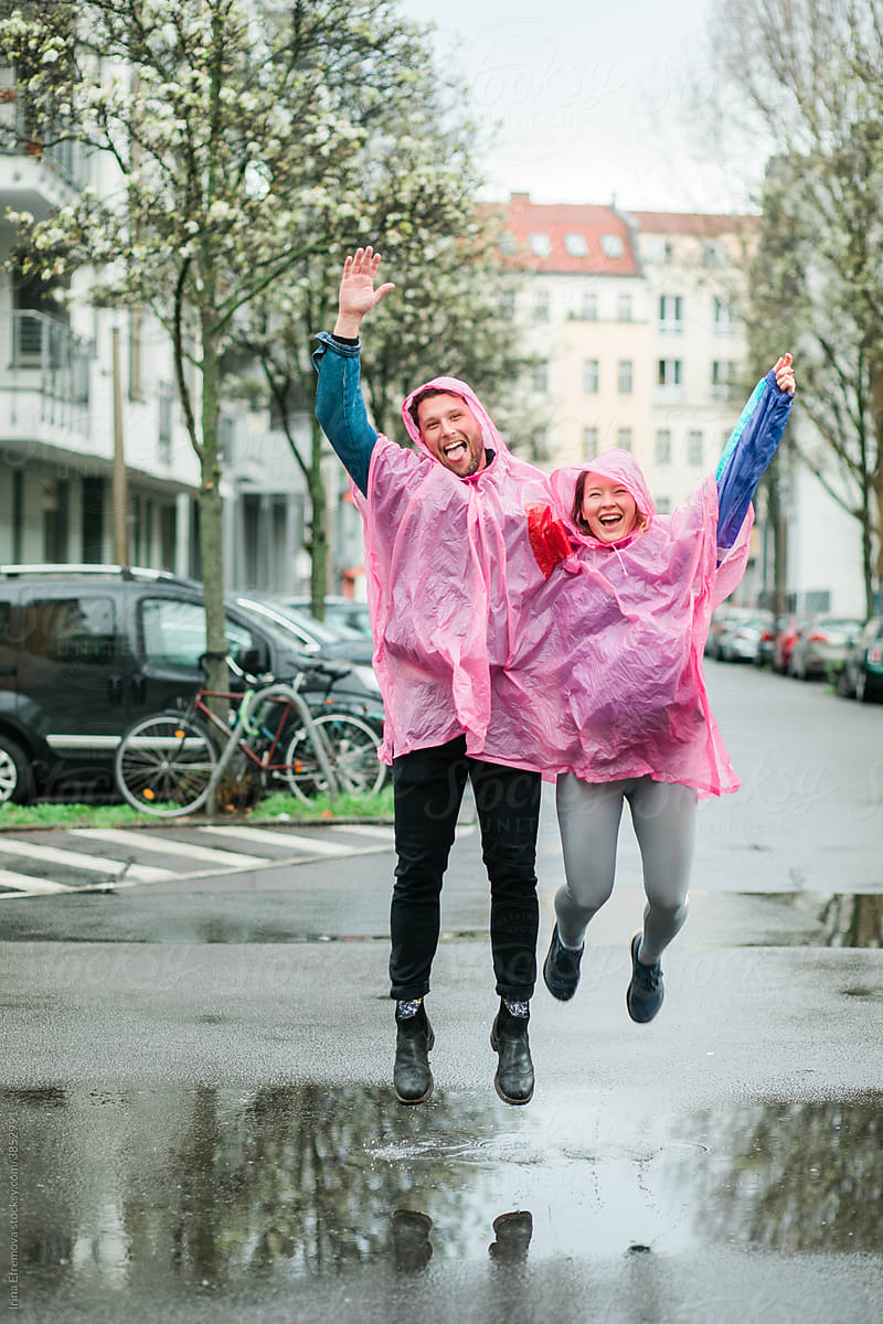 Couple in pink raincoat jumping in rain puddle