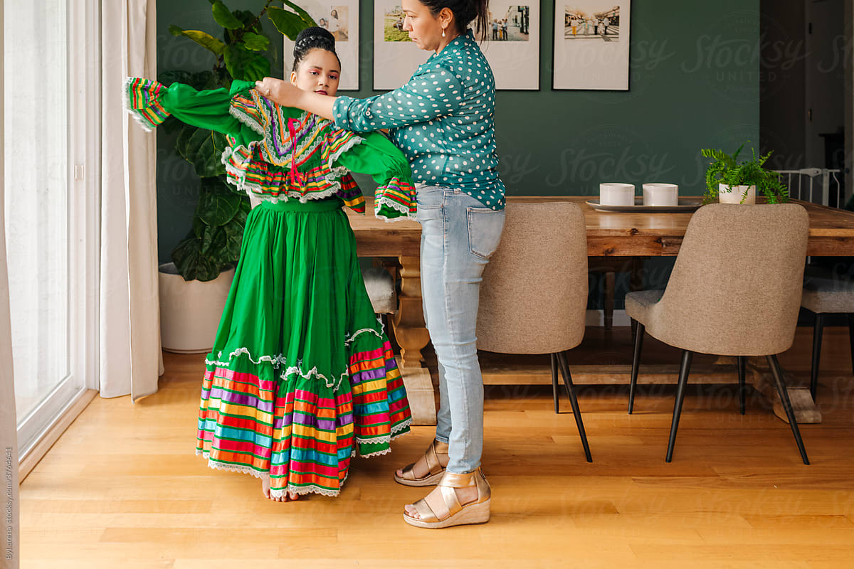 Mother helping daughter to dress up for a traditional Mexican perfomance