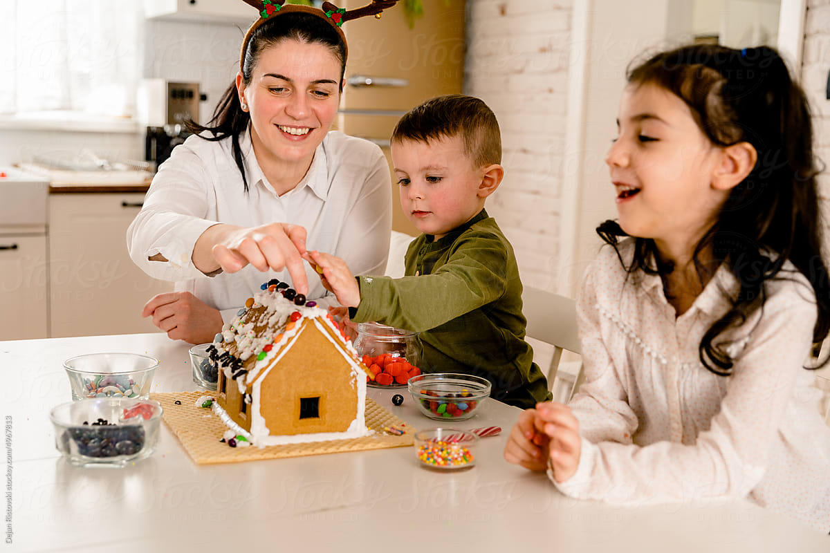 Cheerful family decorating Gingerbread house