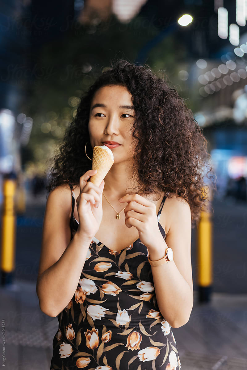 A woman eats icecream at night on the street