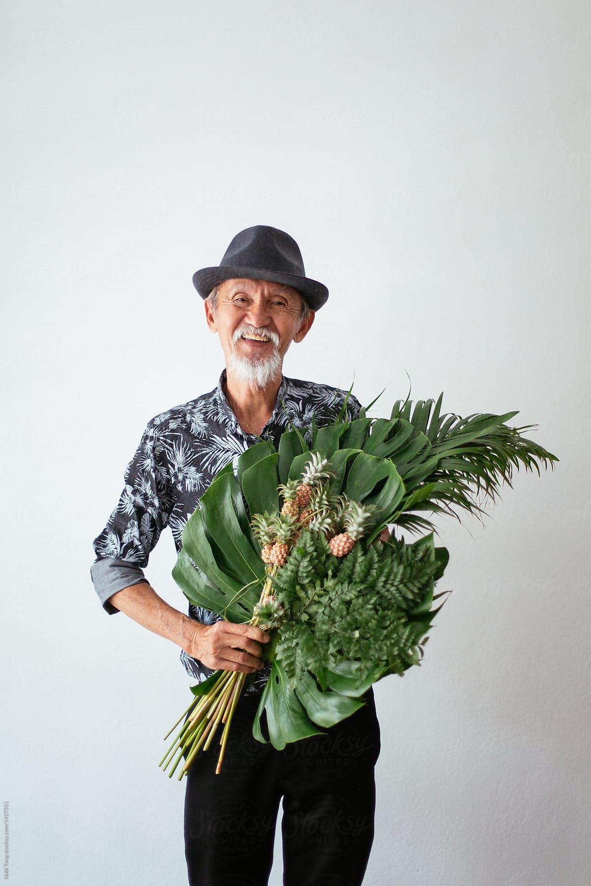Happy asian old man holding tropical bouquet and mini pineapple