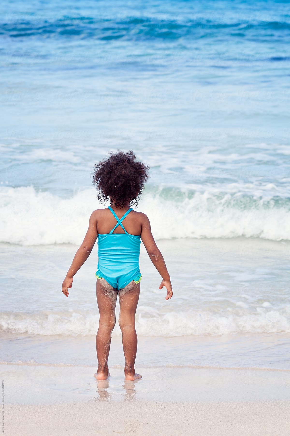 Girl in a bright blue bathing suit watching the waves