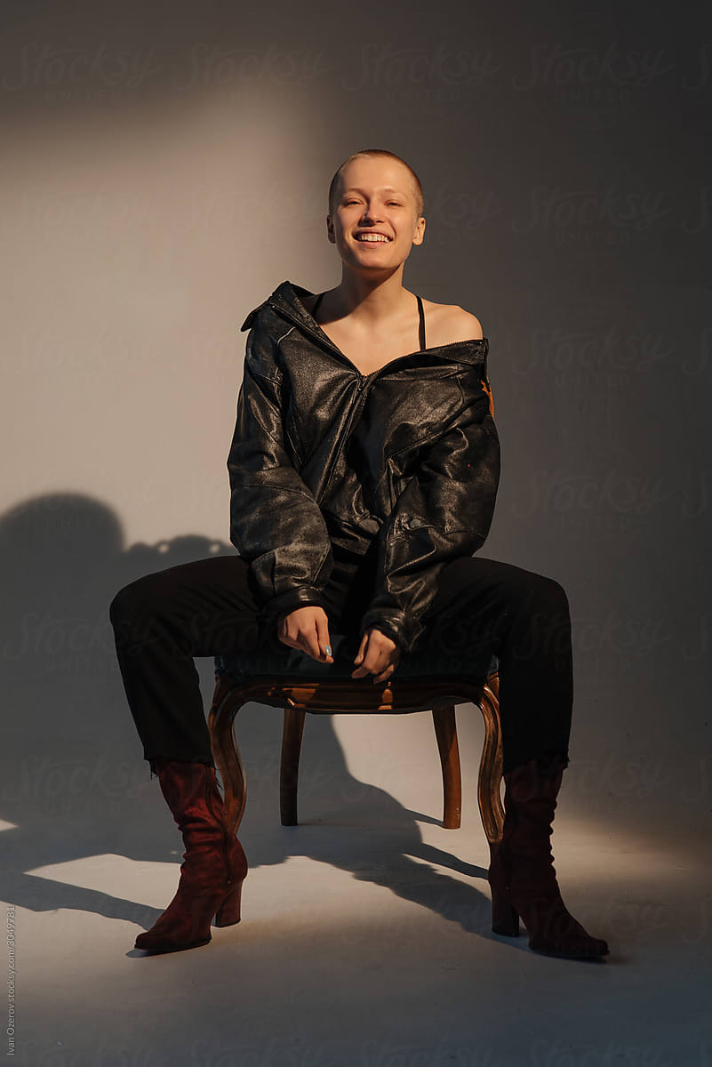 studio portrait of a beautiful bald girl in a leather jacket sitting on a chair