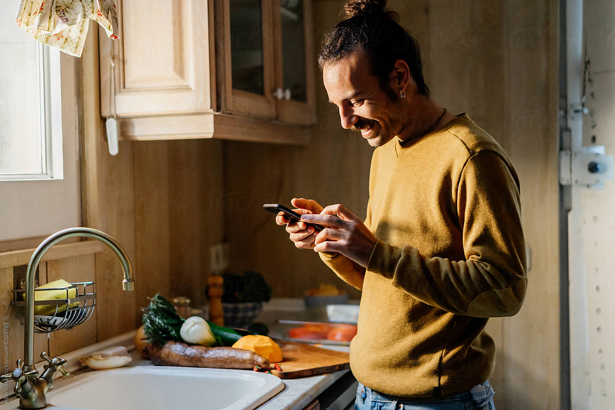 Young man looking at phone in kitchen while cooking