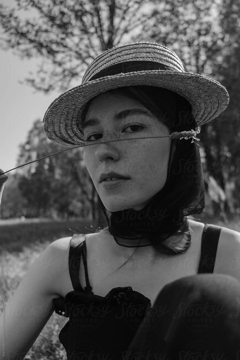 black and white portrait of a girl in a dress and a hat sitting on the grass