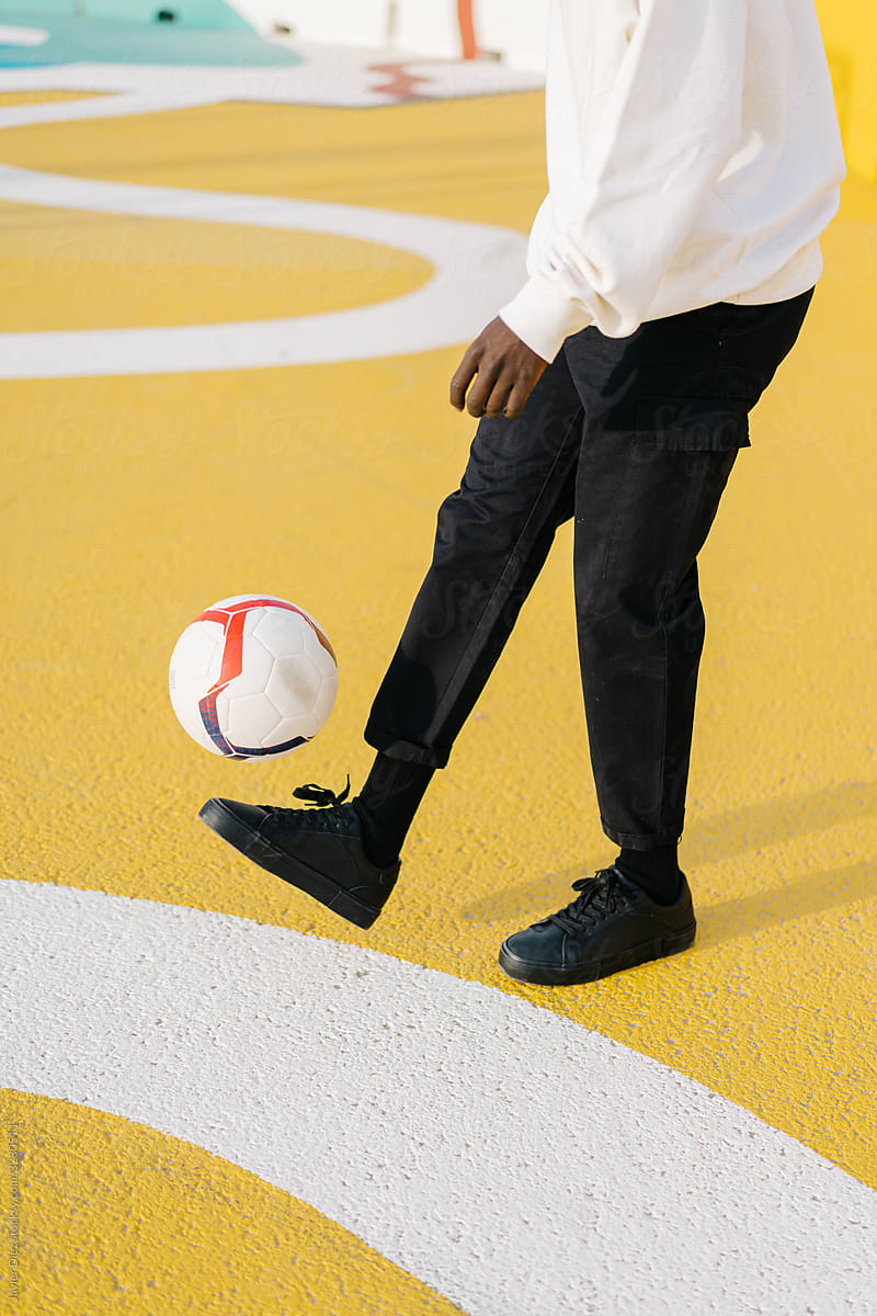 Black man in casual wear kicking ball on playground