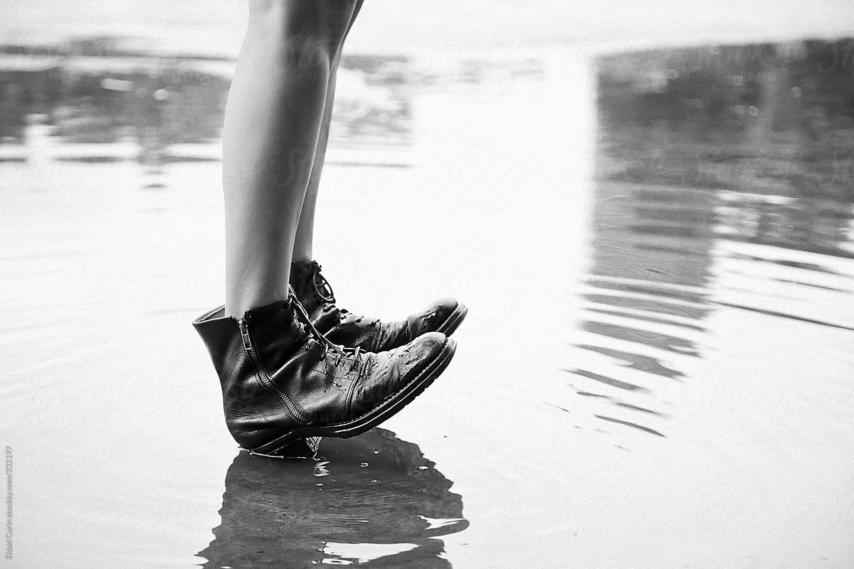 Legs in Black Boots in Calm Puddle