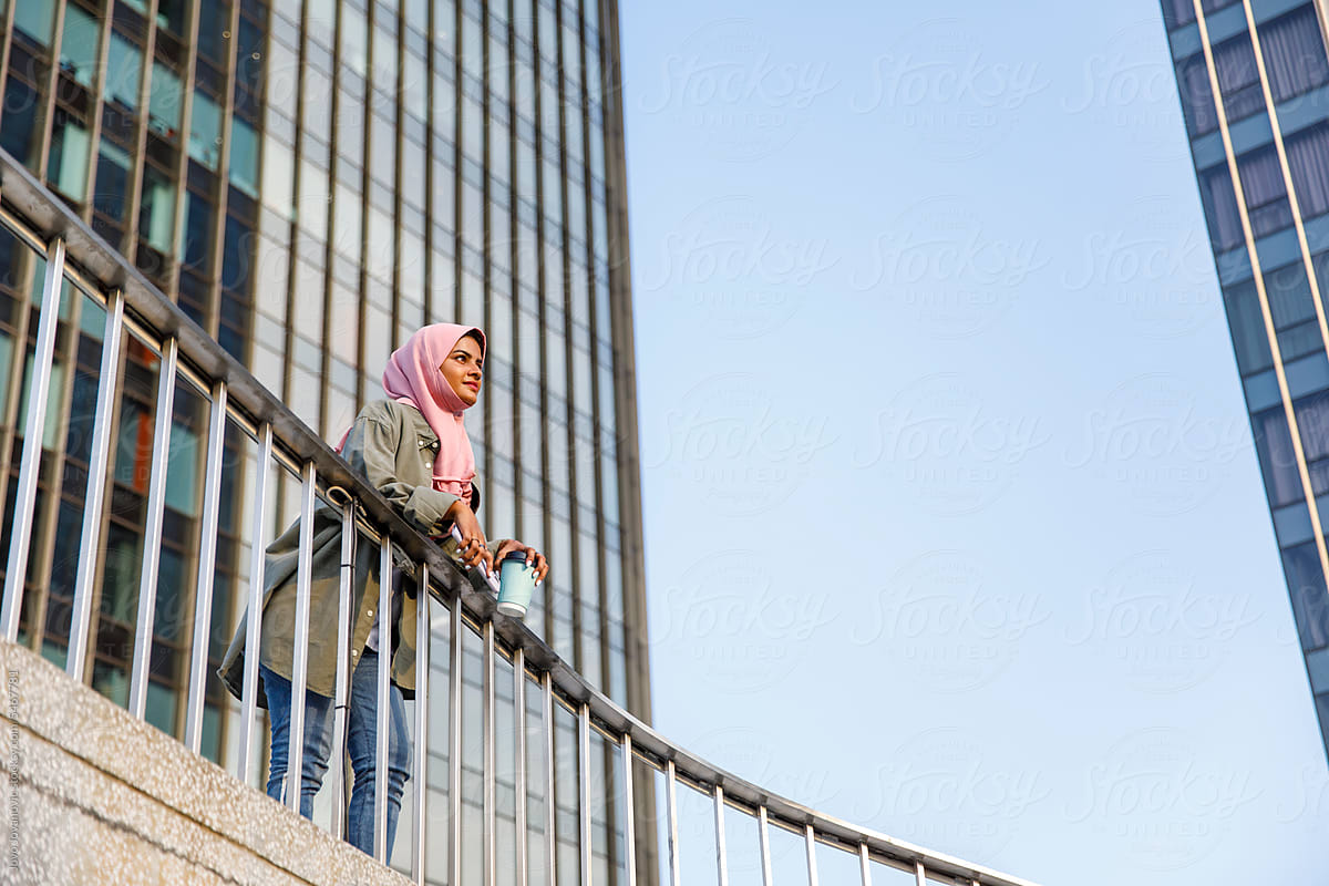 Woman in headscarf holding coffee cup and admiring city