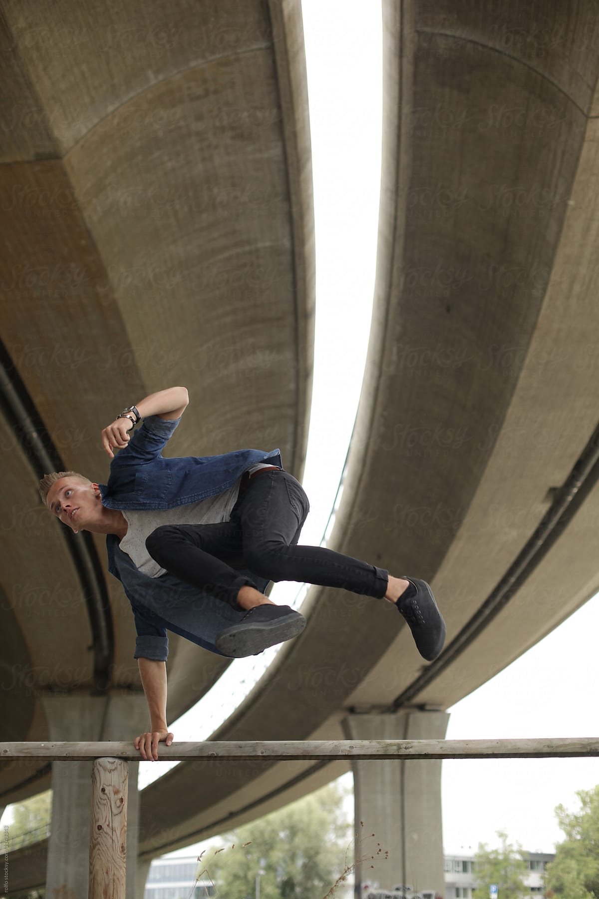 Young man jumping over wooden railing under motorway