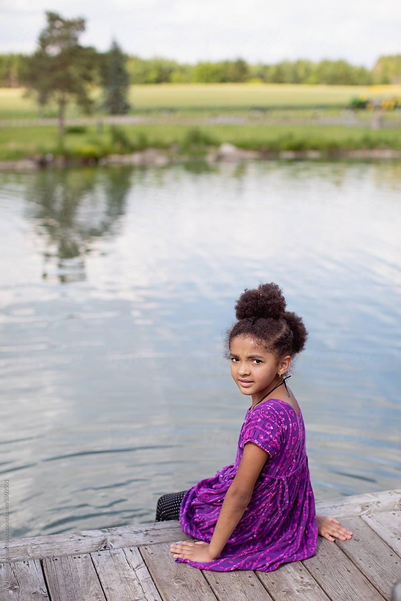 Girl child sitting on the end of a dock with her feet in the water.