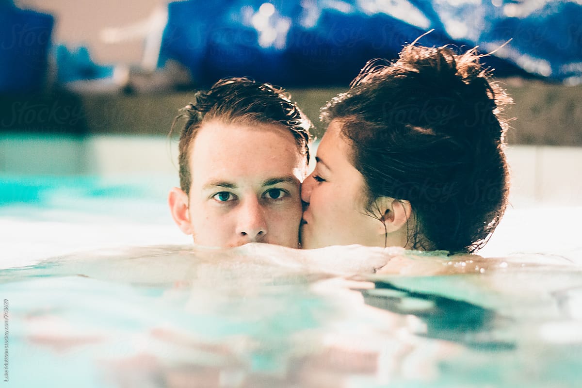 Young Woman Kissing Young Man On Cheek In Swimming Pool