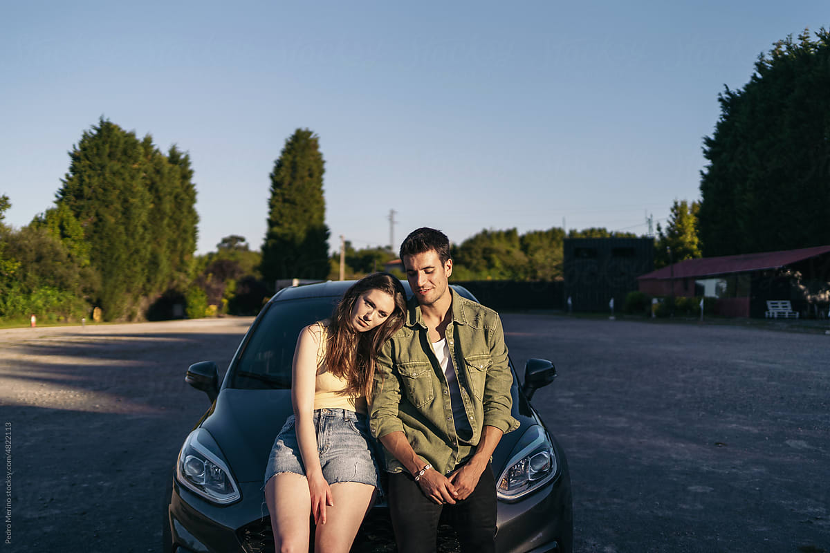 Couple leaning on car at sunset