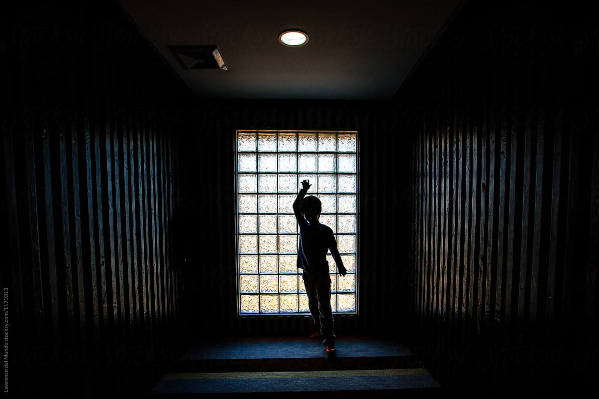 Silhouette of a young boy having fun in a dark hallway.