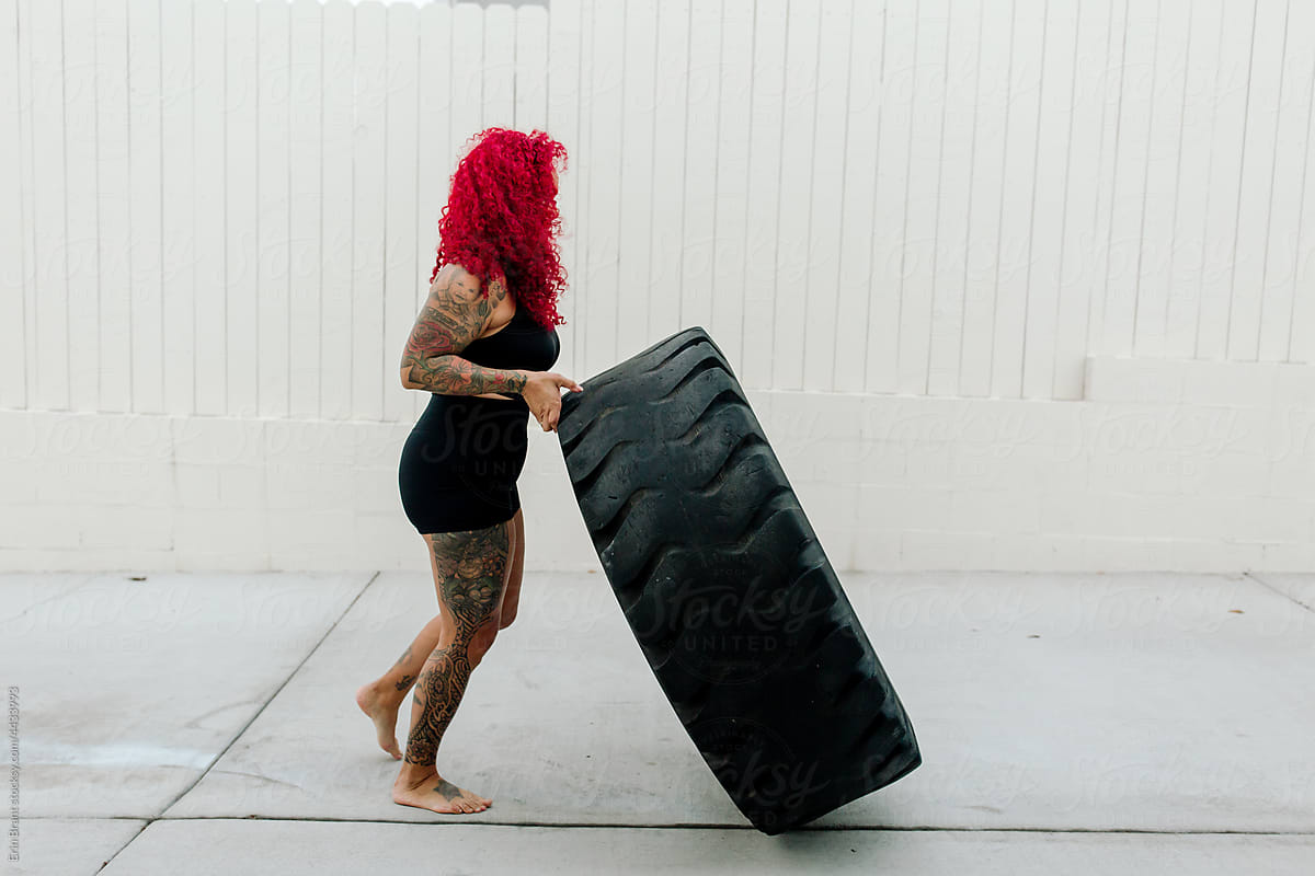 Muscular redhead pushing large tire