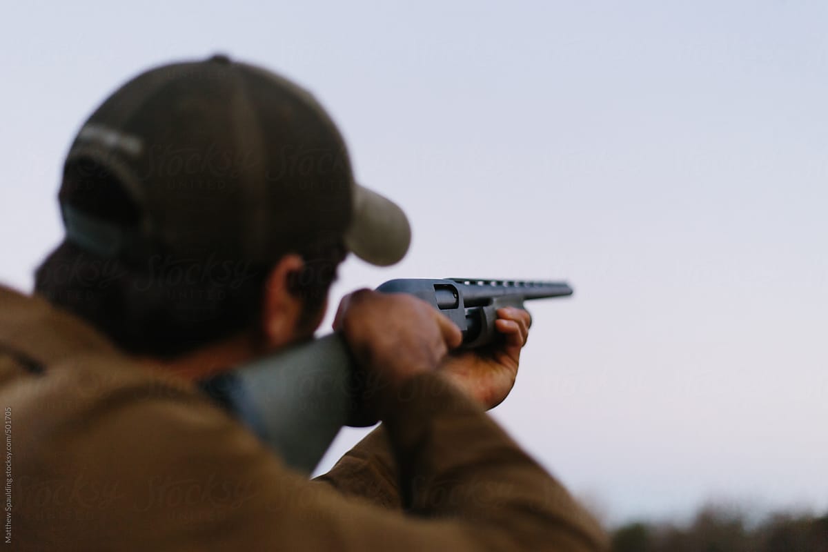 Person aiming gun at target and shooting shotgun