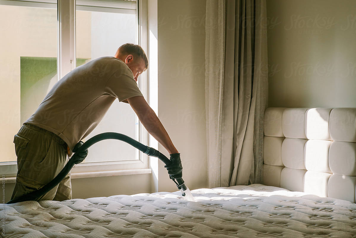 A man is dry-cleaning the mattress in the bedroom