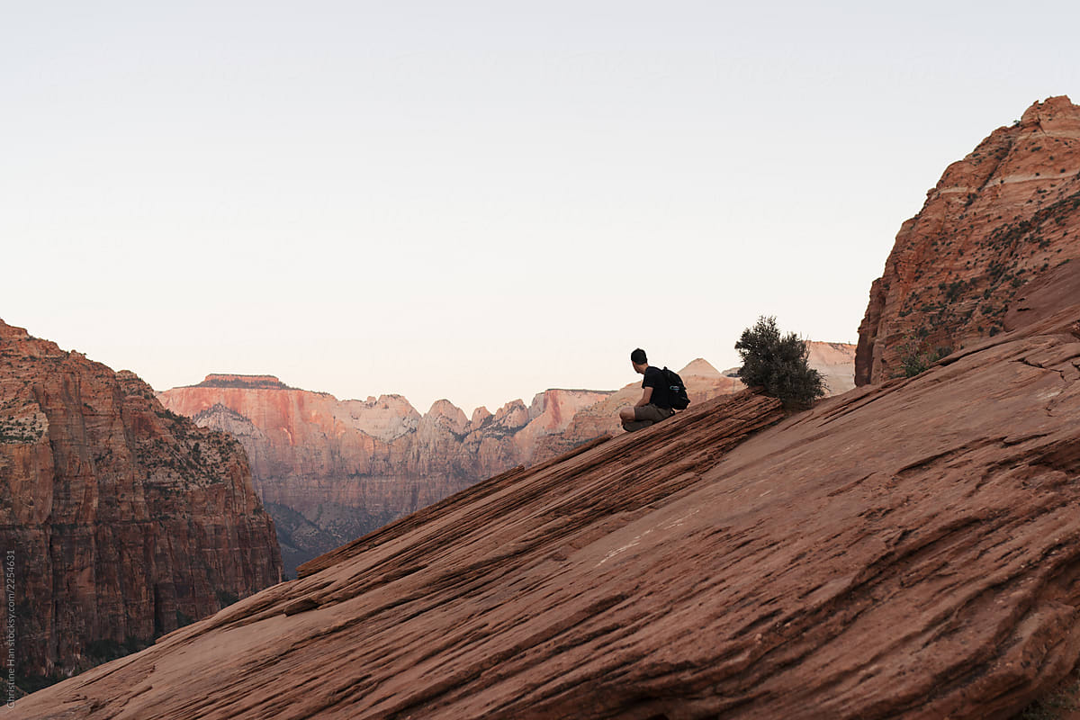 Male hiker taking a break and enjoying the view of beautiful canyons in a rugged desert landscape at sunrise