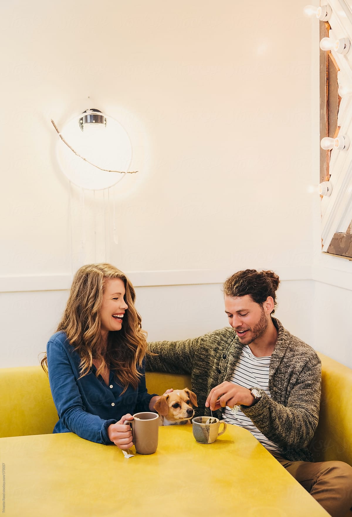 Couple laughing at dining room table with tea and their dog