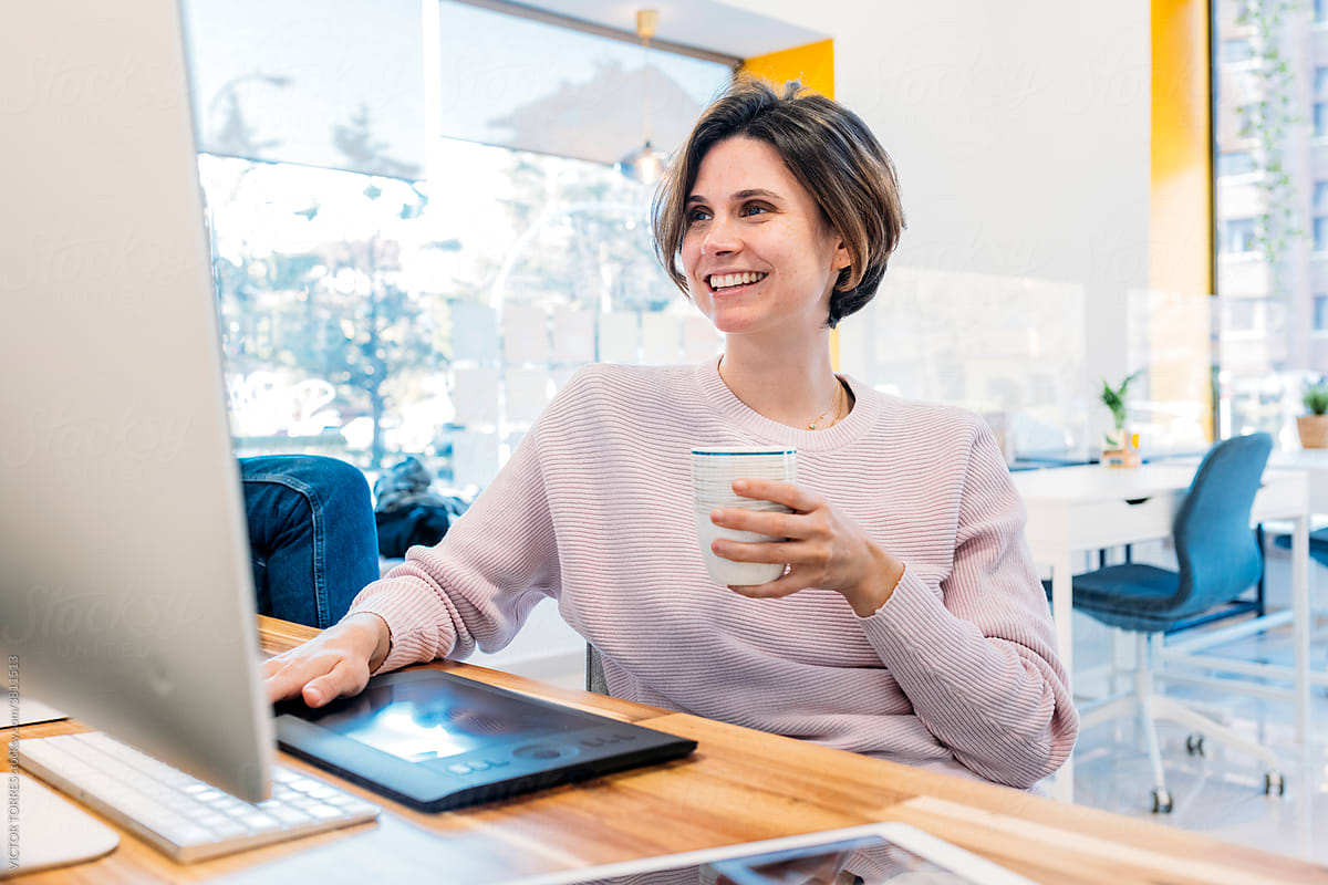 Smiling woman with mug working on computer