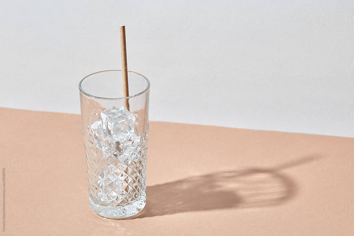 Glass with ice cubes and paper straw.