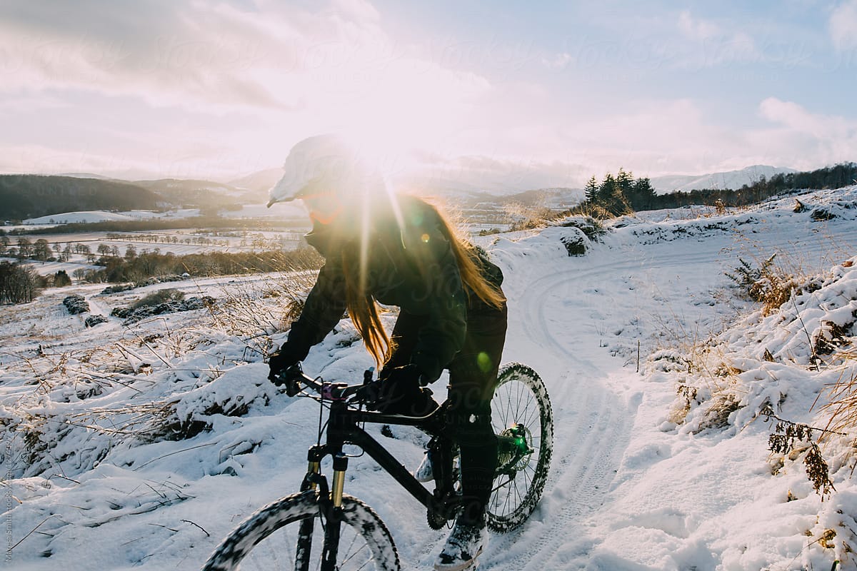 Golden hour sun-flare over a female mountain biker, cycling a snowy trail