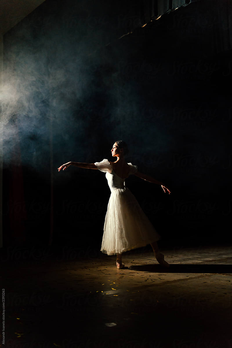 Ballerina in dress stretching on scene in darkness