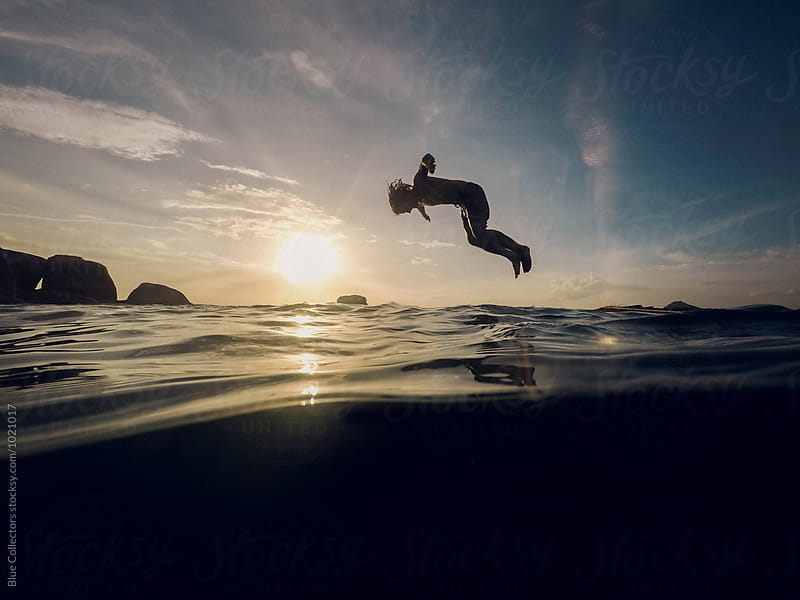 Young sport man jumping to the water from the floating platform of bamboo in the sea sunset