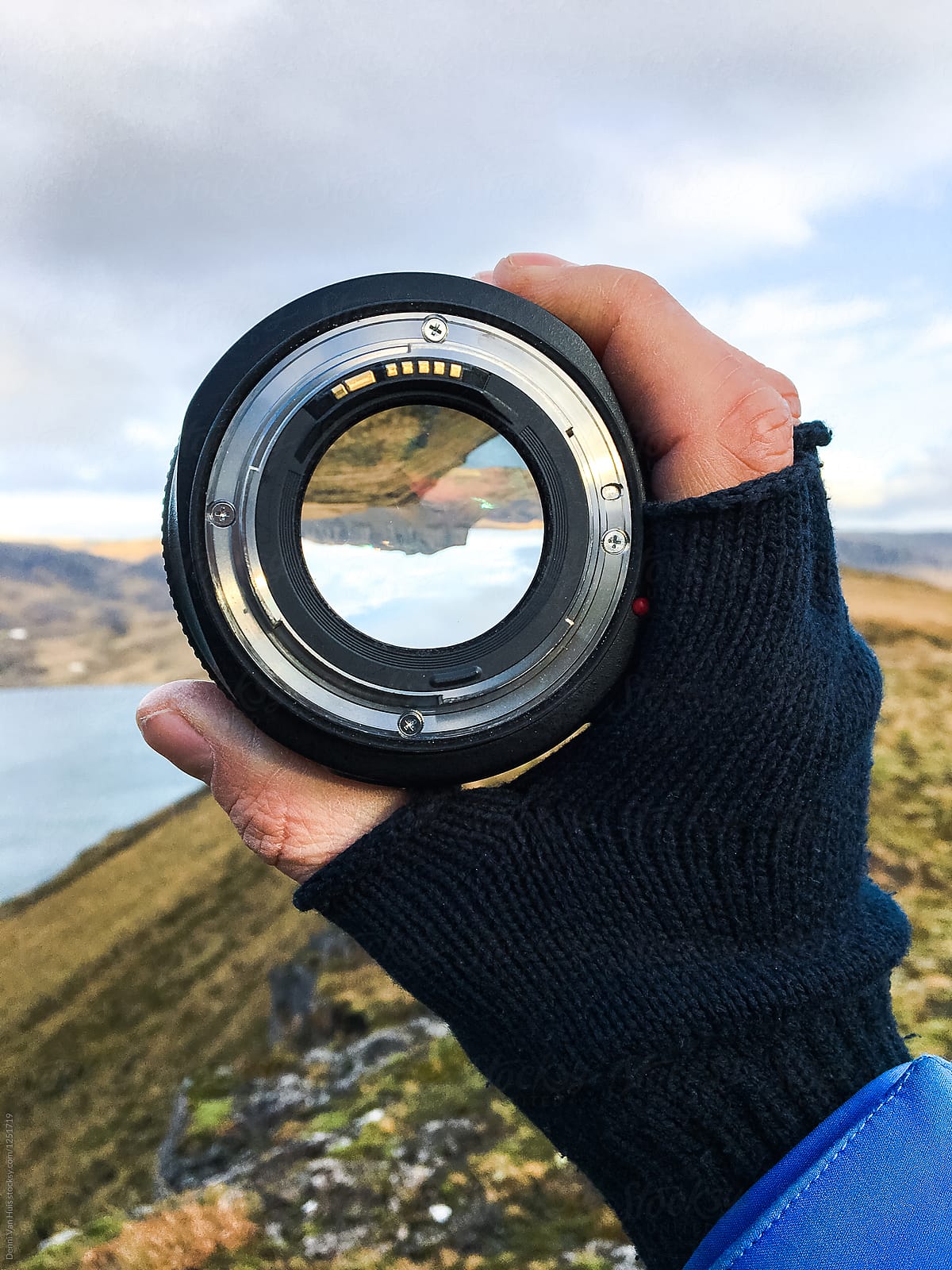 Hand with glove holding up a camera lens and looks through it surrounded by a beautiful landscape
