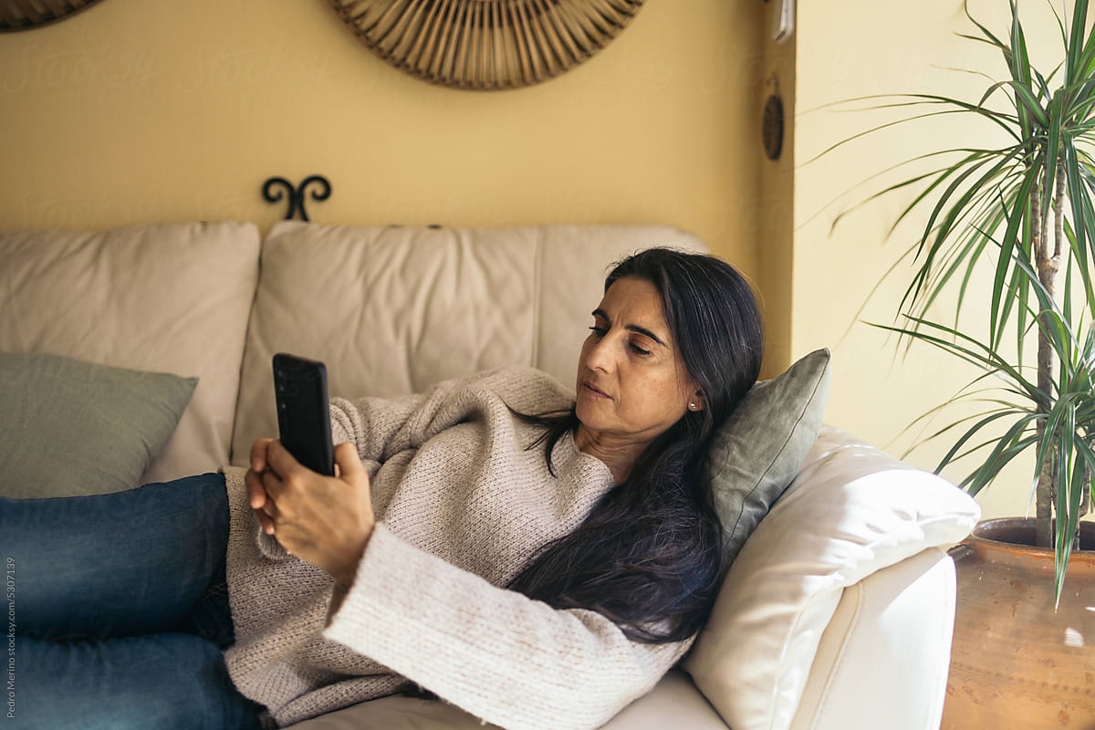 Relaxed woman at home using smartphone lying on sofa
