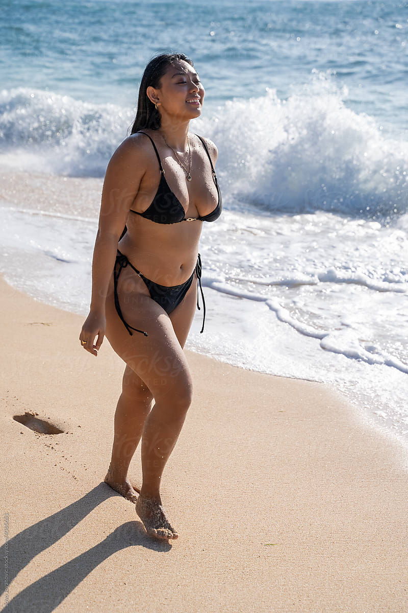 Curvy Woman Confidently Walking Down Beach In Bikini by Stocksy